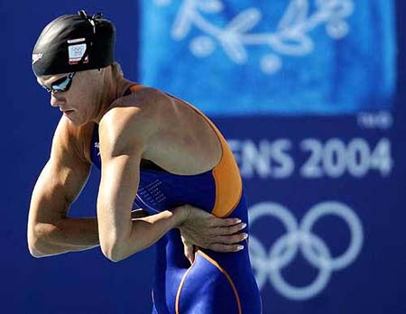 Olympic swimmer at Athens 2004 bent forward in a focused pre-race back and shoulder stretch