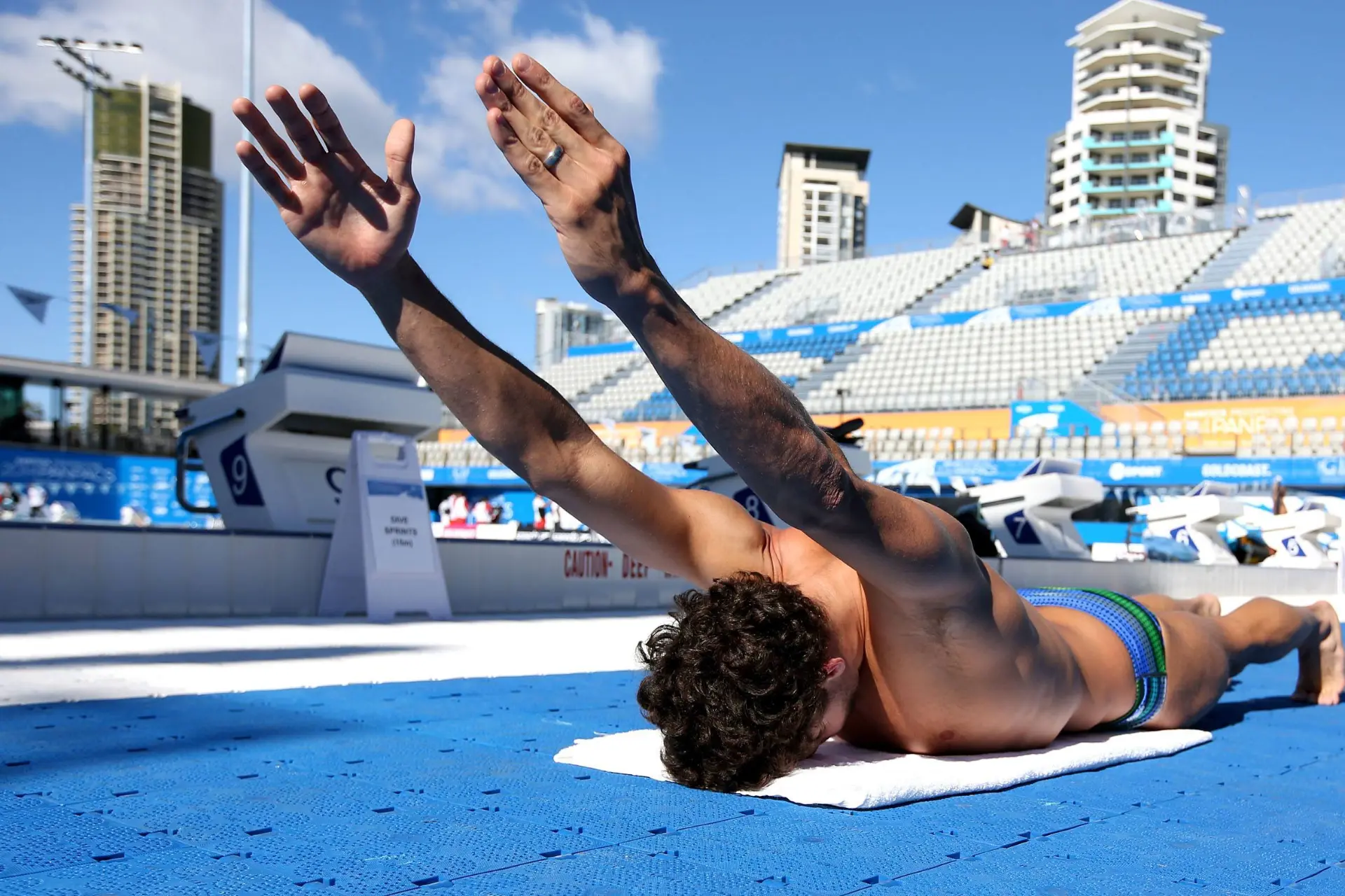 Swimmer lying prone on a pool deck, arms raised high into a streamline position, showing exceptional shoulder mobility